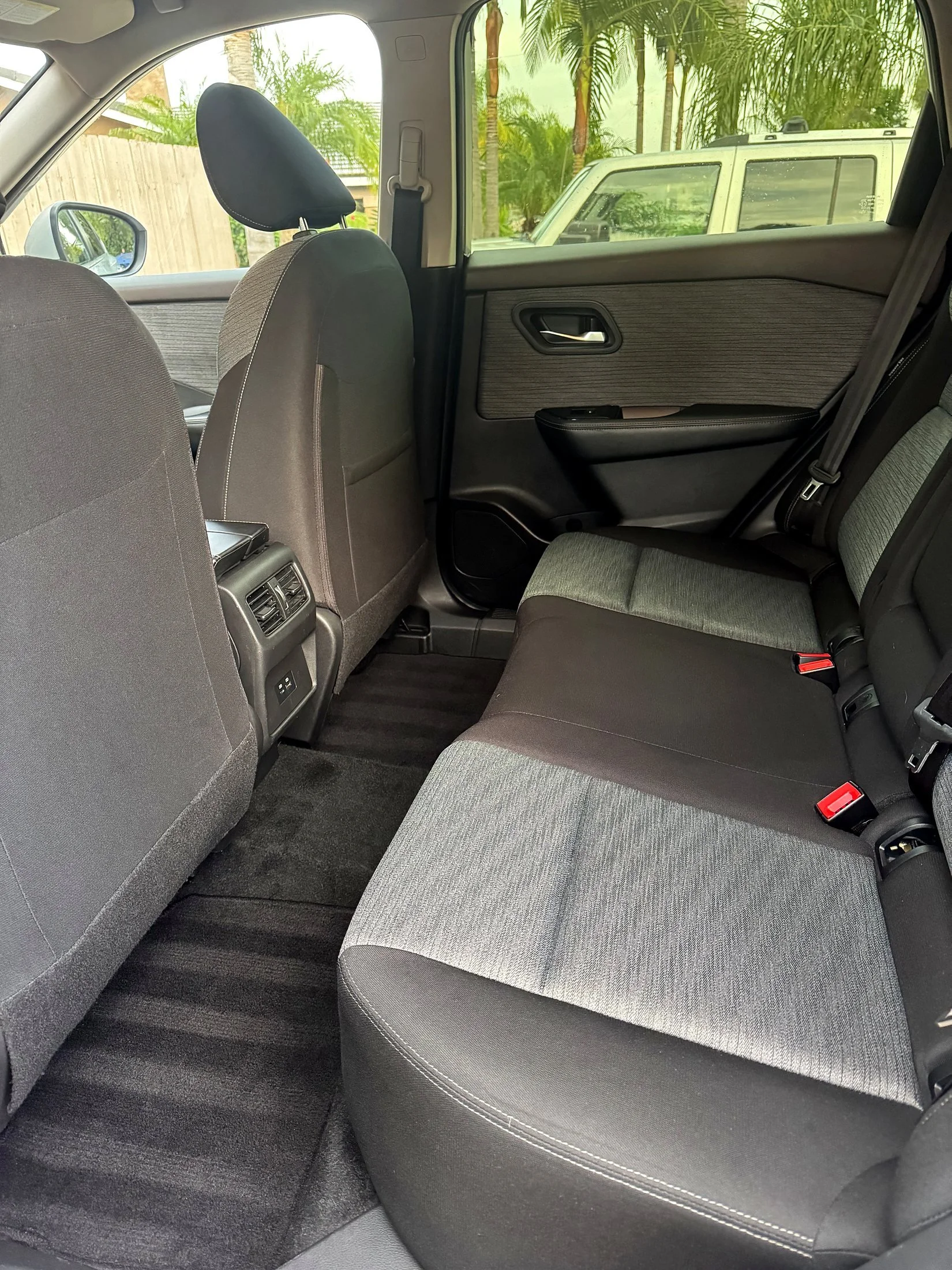Interior of a vehicle showing the back seat, front seats, and side windows with a view of greenery and a white vehicle outside.