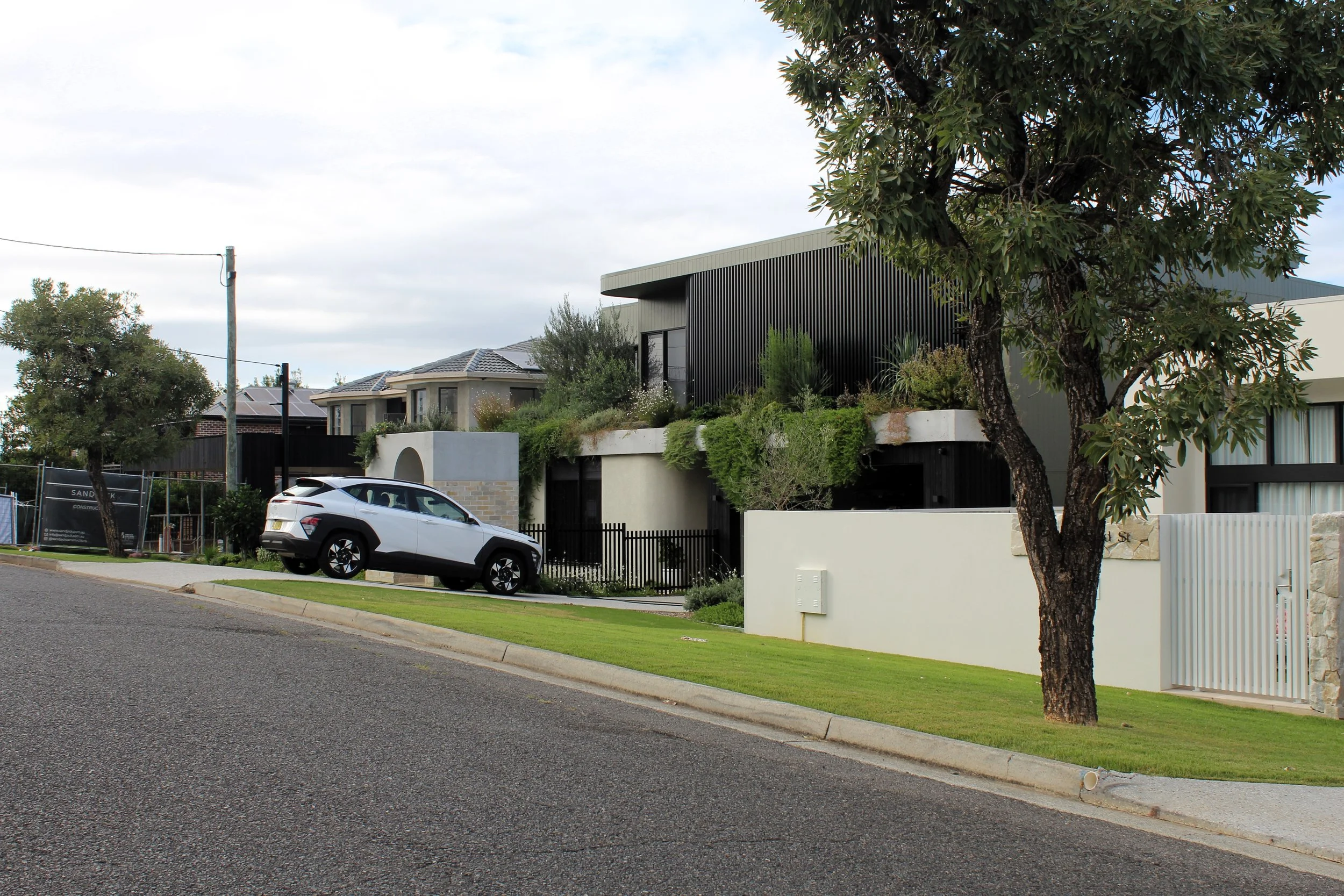 Modern residential houses with greenery and parked car on a suburban street.