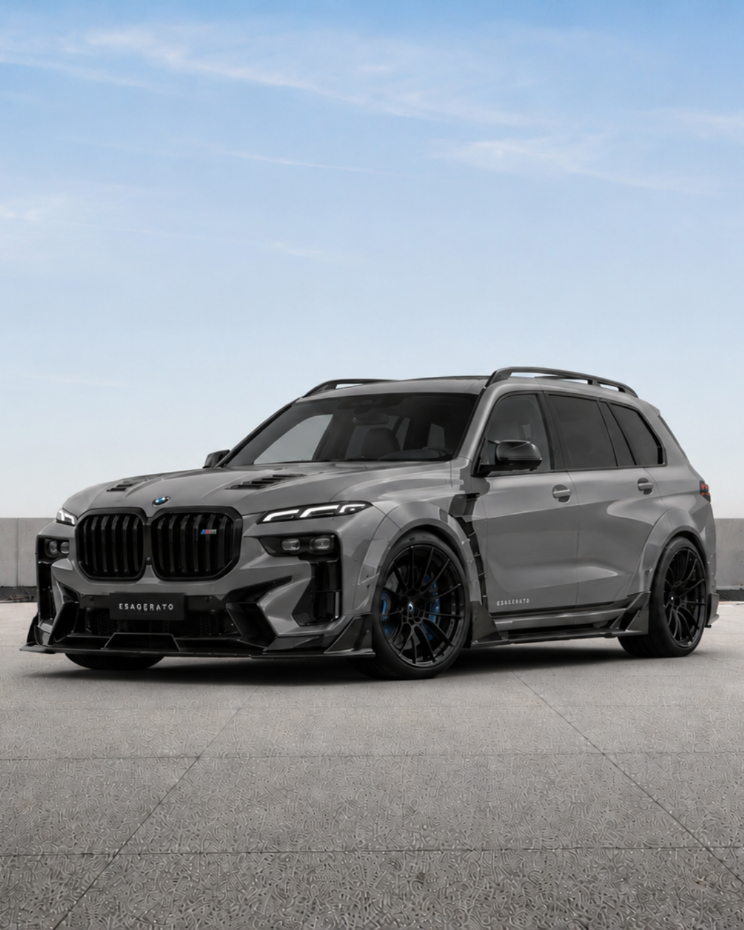 A black and gray Esagerato BMW luxury SUV with custom wheels, black grille, and sporty design, parked on a concrete surface under a clear blue sky.