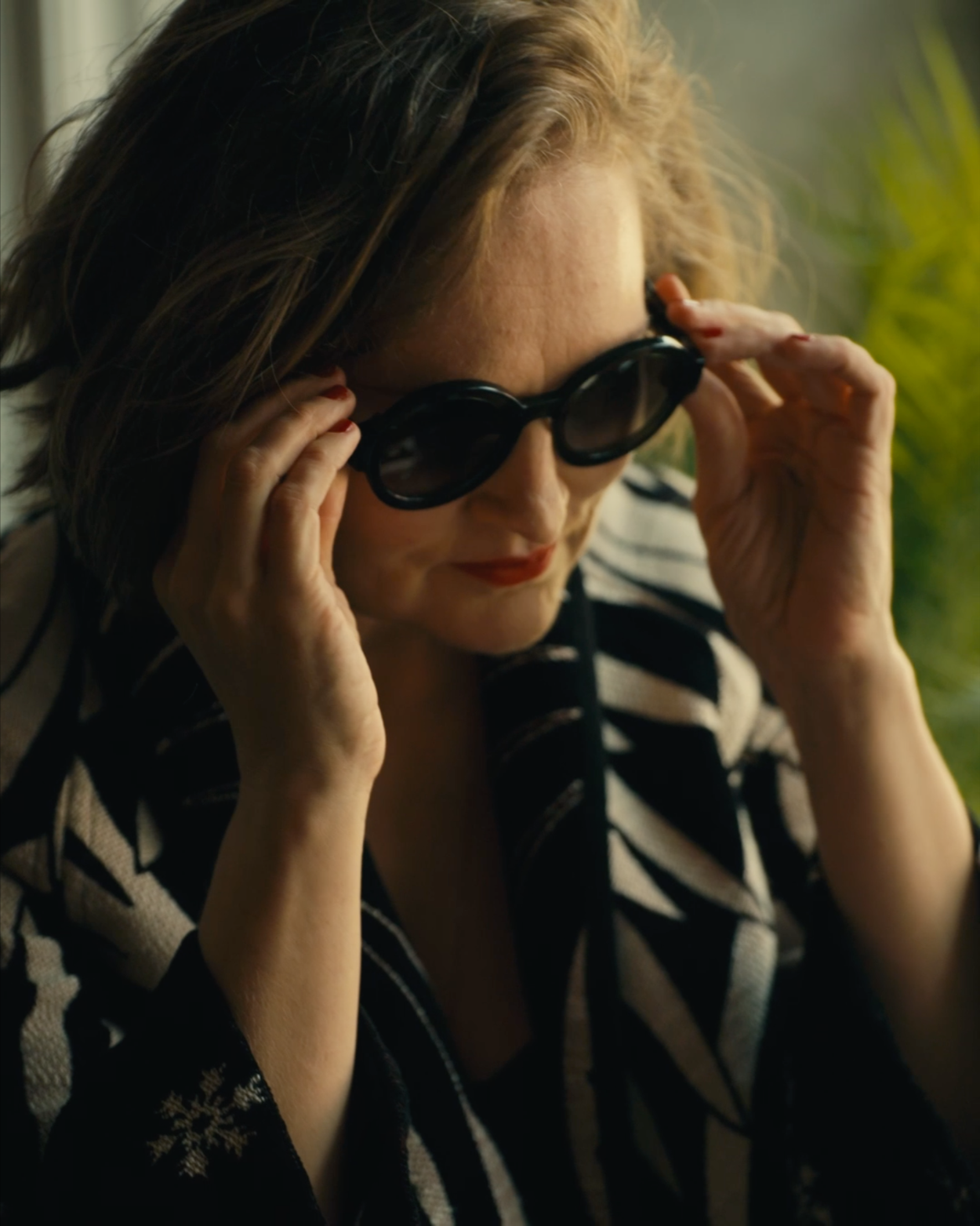 A woman with brown hair wearing a black and white striped blazer and sunglasses.