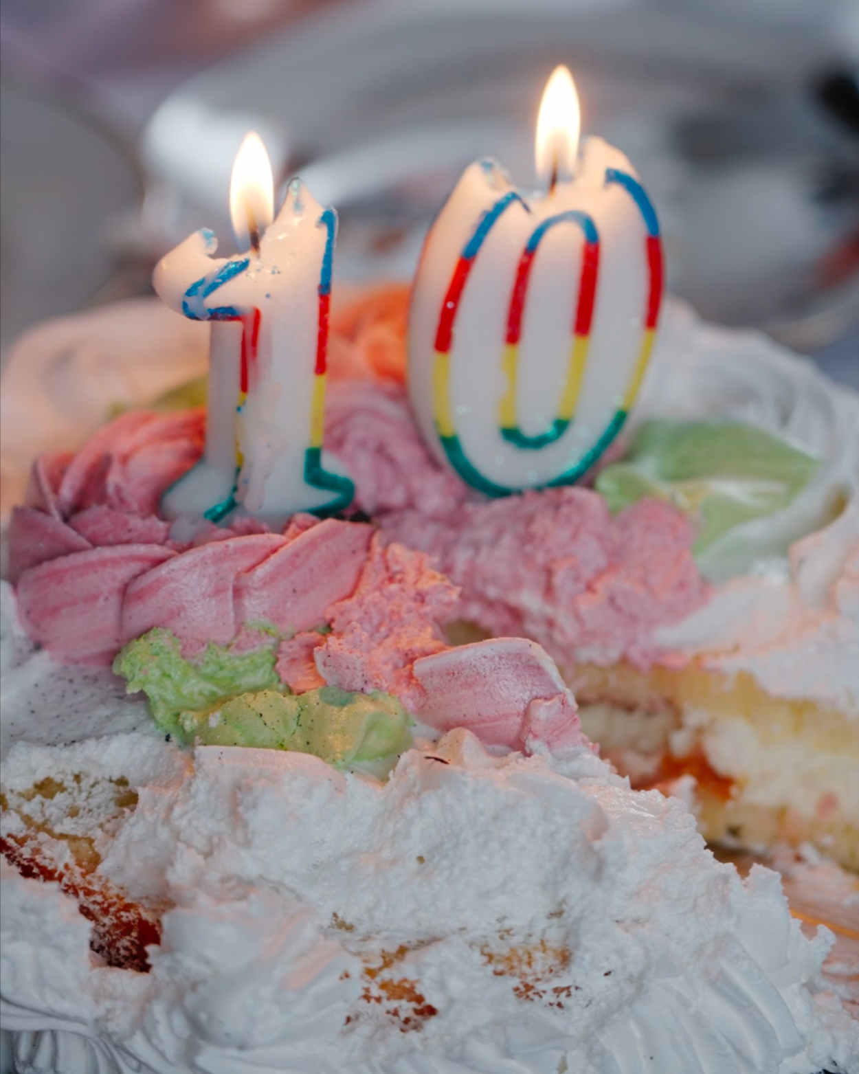 Close-up of a birthday cake with colorful frosting and two lit candles shaped as the number 10.