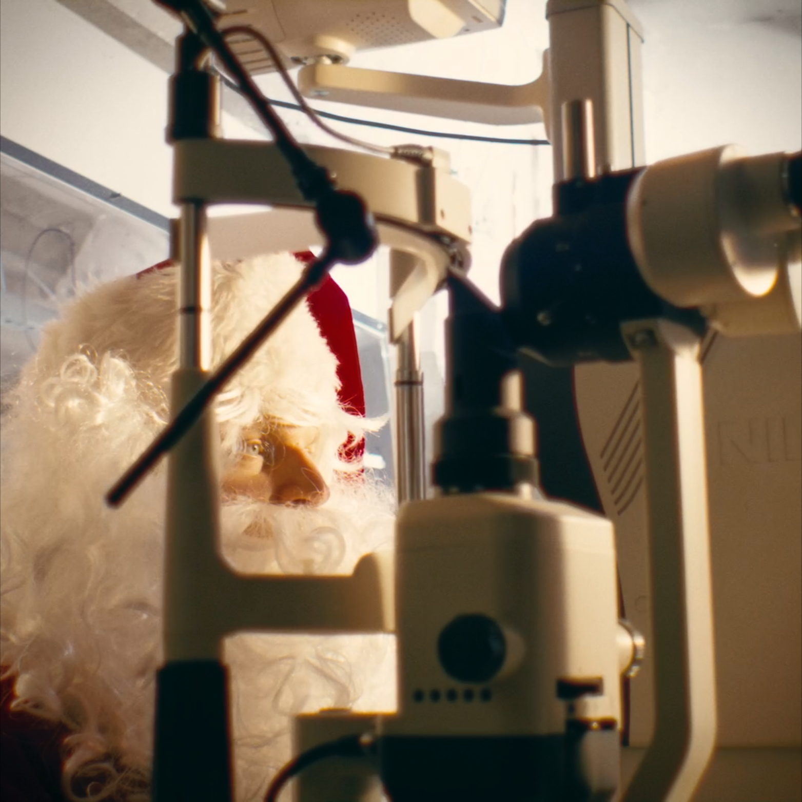 Close-up of a mechanical device with wires and a white and beige frame, with a blurry Santa Claus figurine in the background.