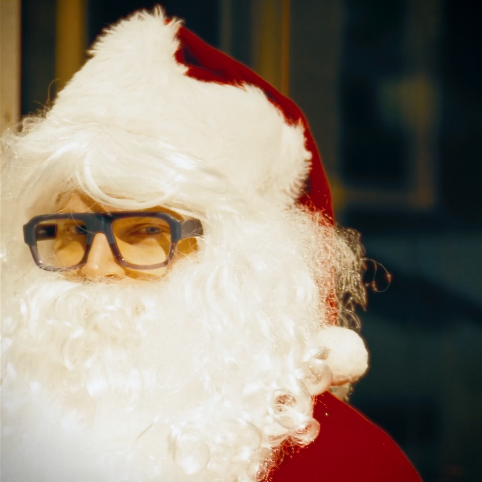 Close-up of Santa Claus with white beard, glasses, and red hat, partially covered in soap bubbles or foam.