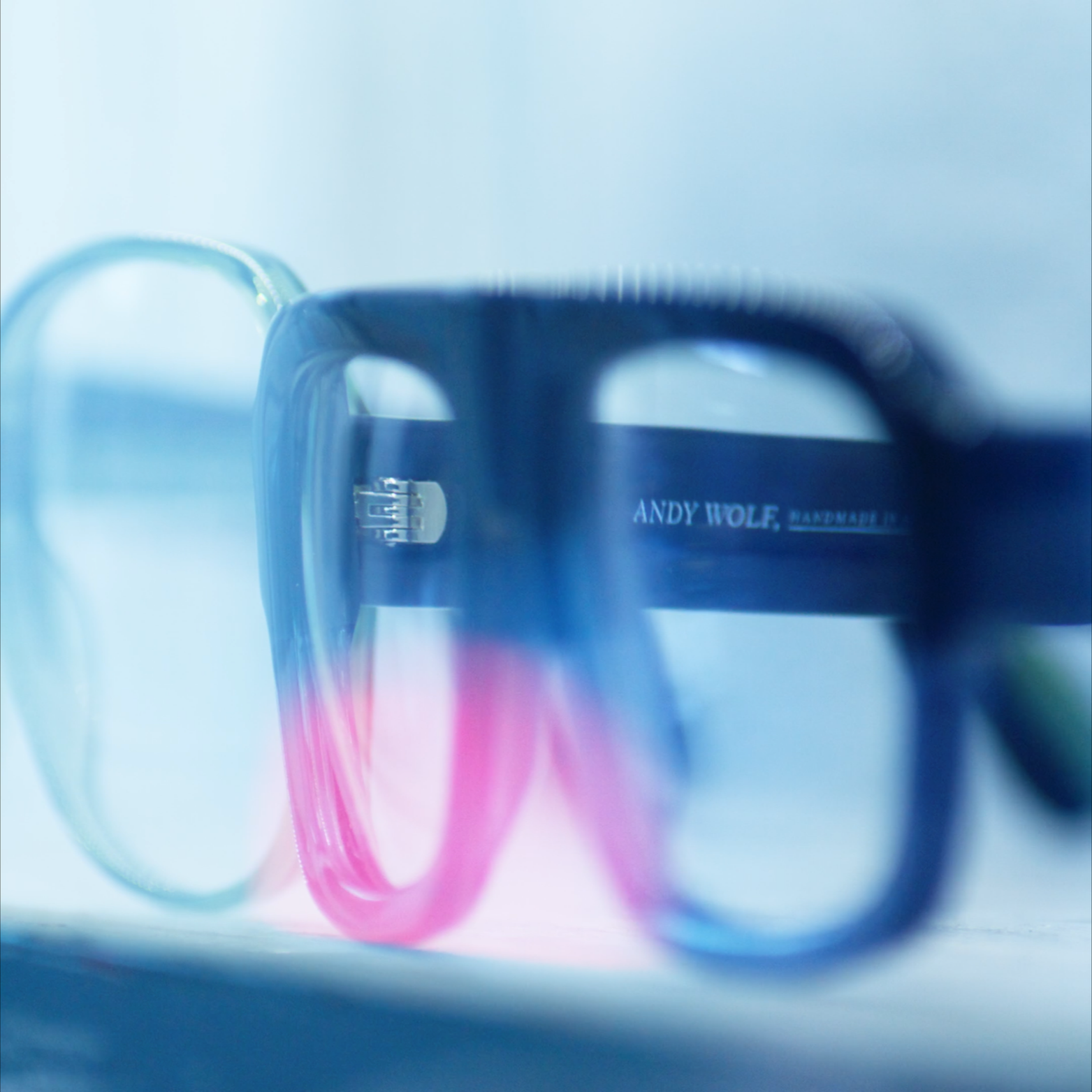 Close-up of a black mug with the text 'Andy Wolf' on it, with a pair of glasses resting on it and a blurred background