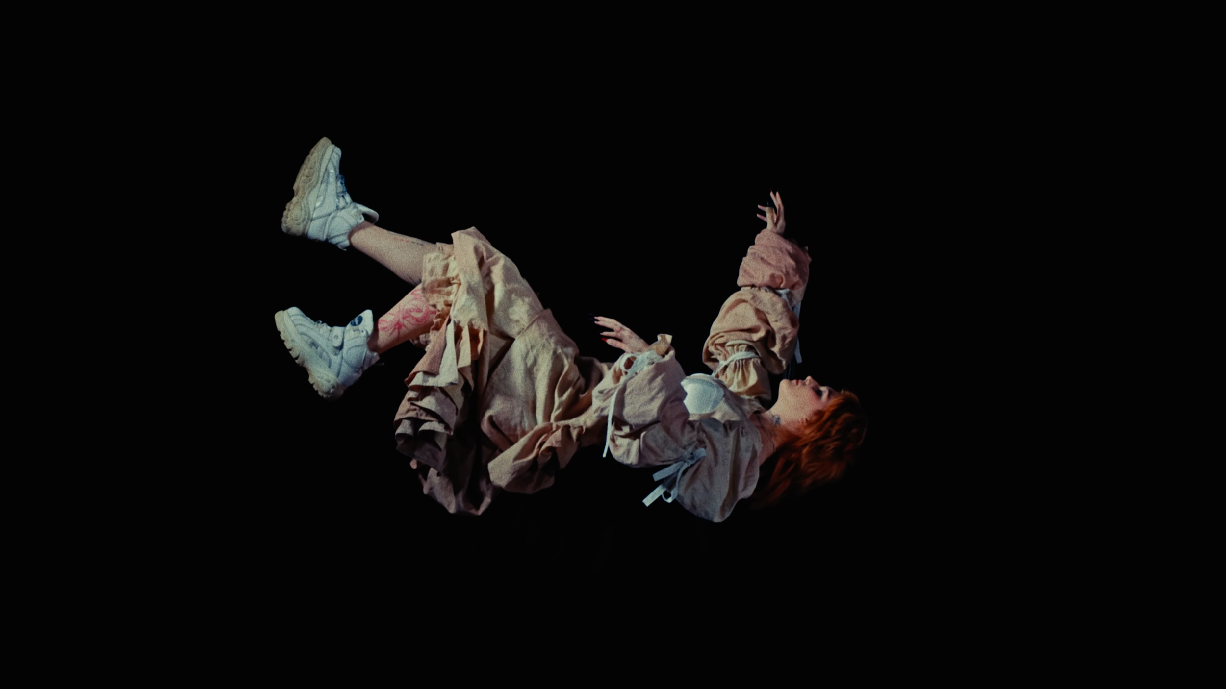 A woman with red hair lying on her back, holding a child above her on a black background.