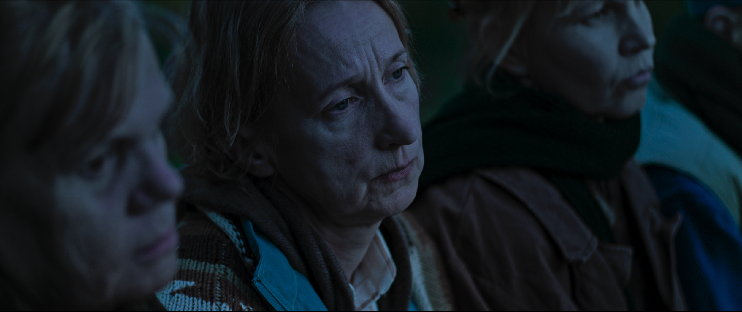 Close-up of four people sitting outdoors at dusk, appearing somber or reflective.