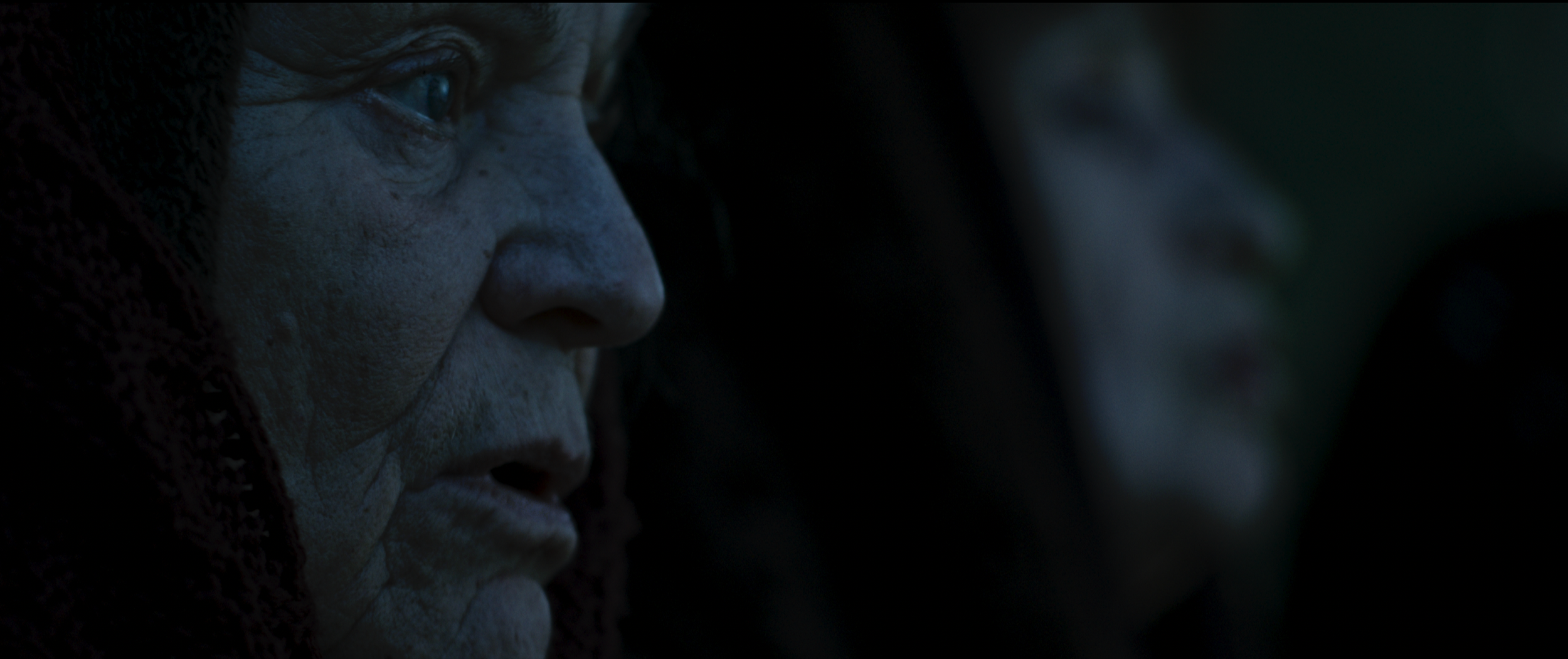 Close-up of a person's face with tribal face paint, looking serious and focused in a dark setting.
