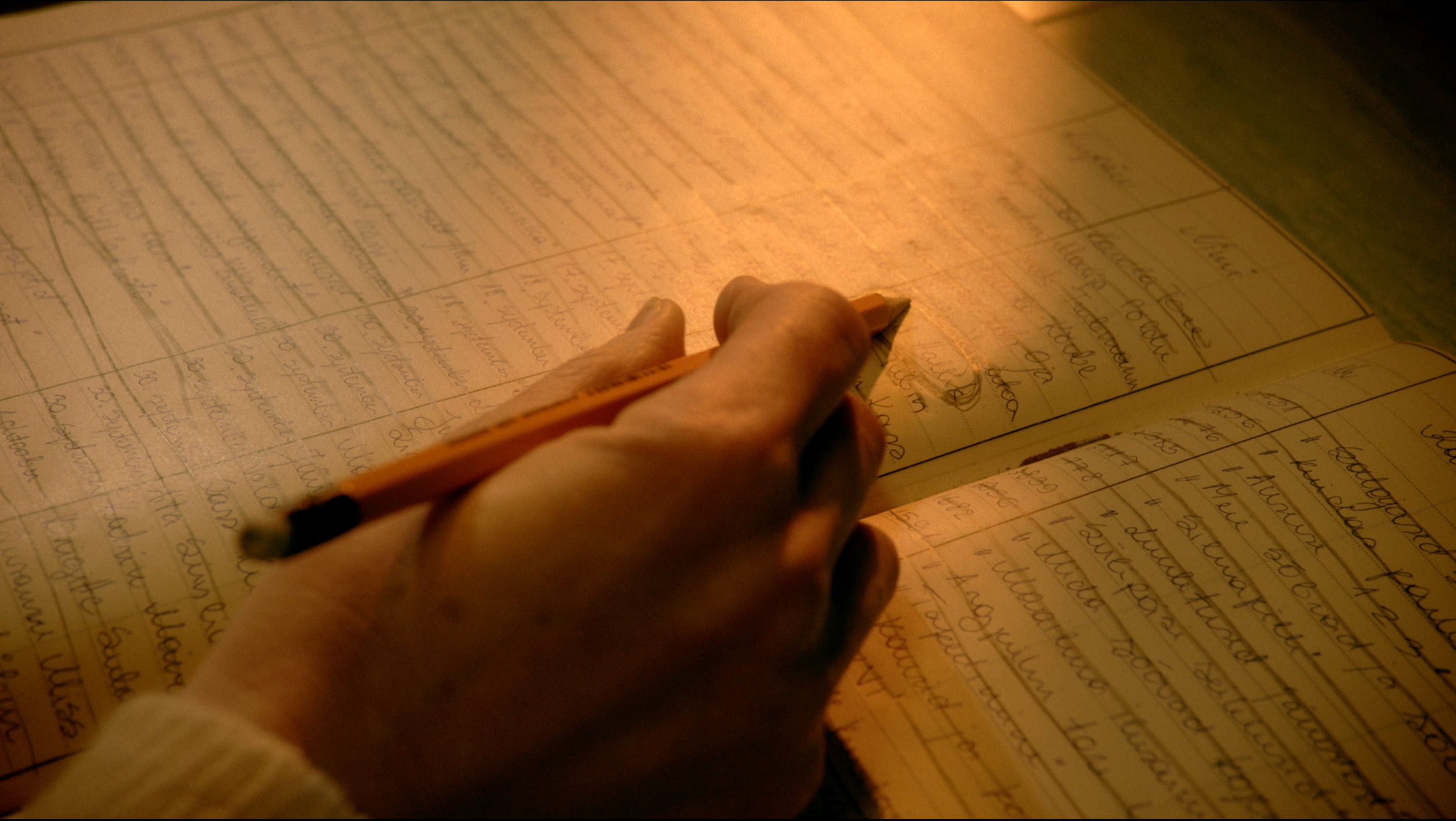 A person writing in a notebook with a pencil under warm light, capturing handwritten text.