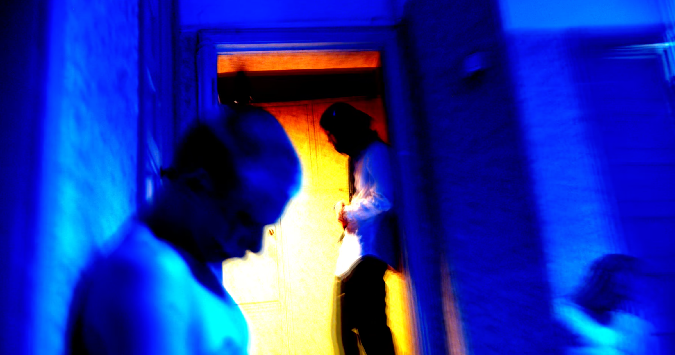Silhouettes of two people against colorful, illuminated background, with blue and orange hues.