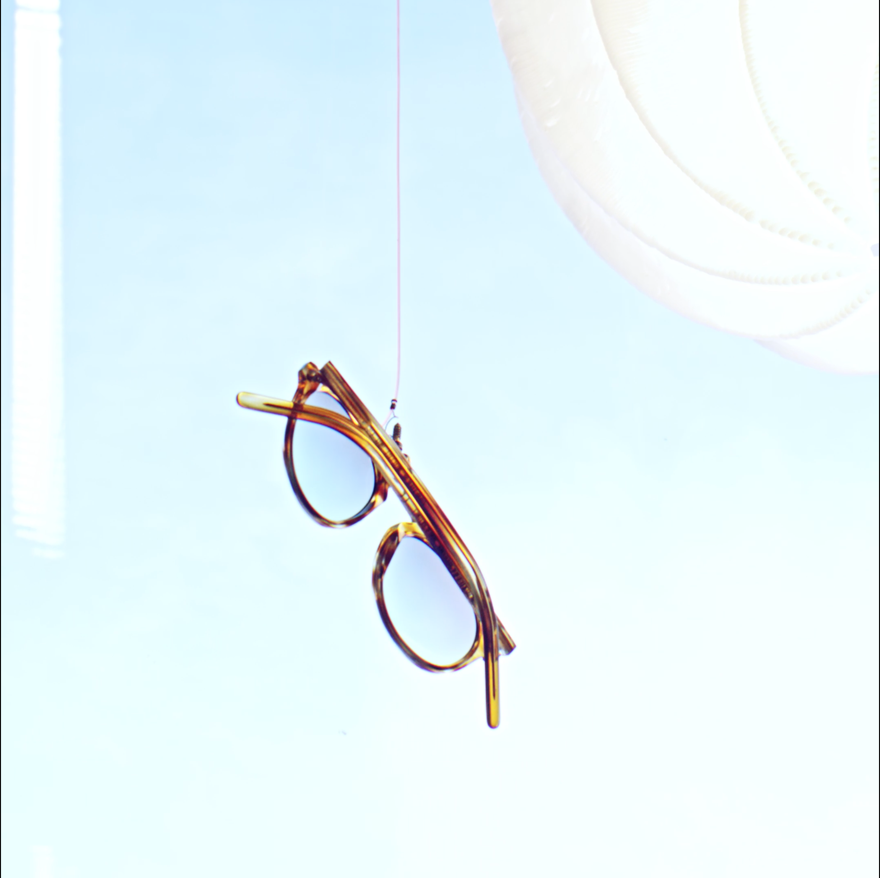 Close-up of a pair of tortoiseshell eyeglasses on a clear surface and a transparent and white seashell in the background.