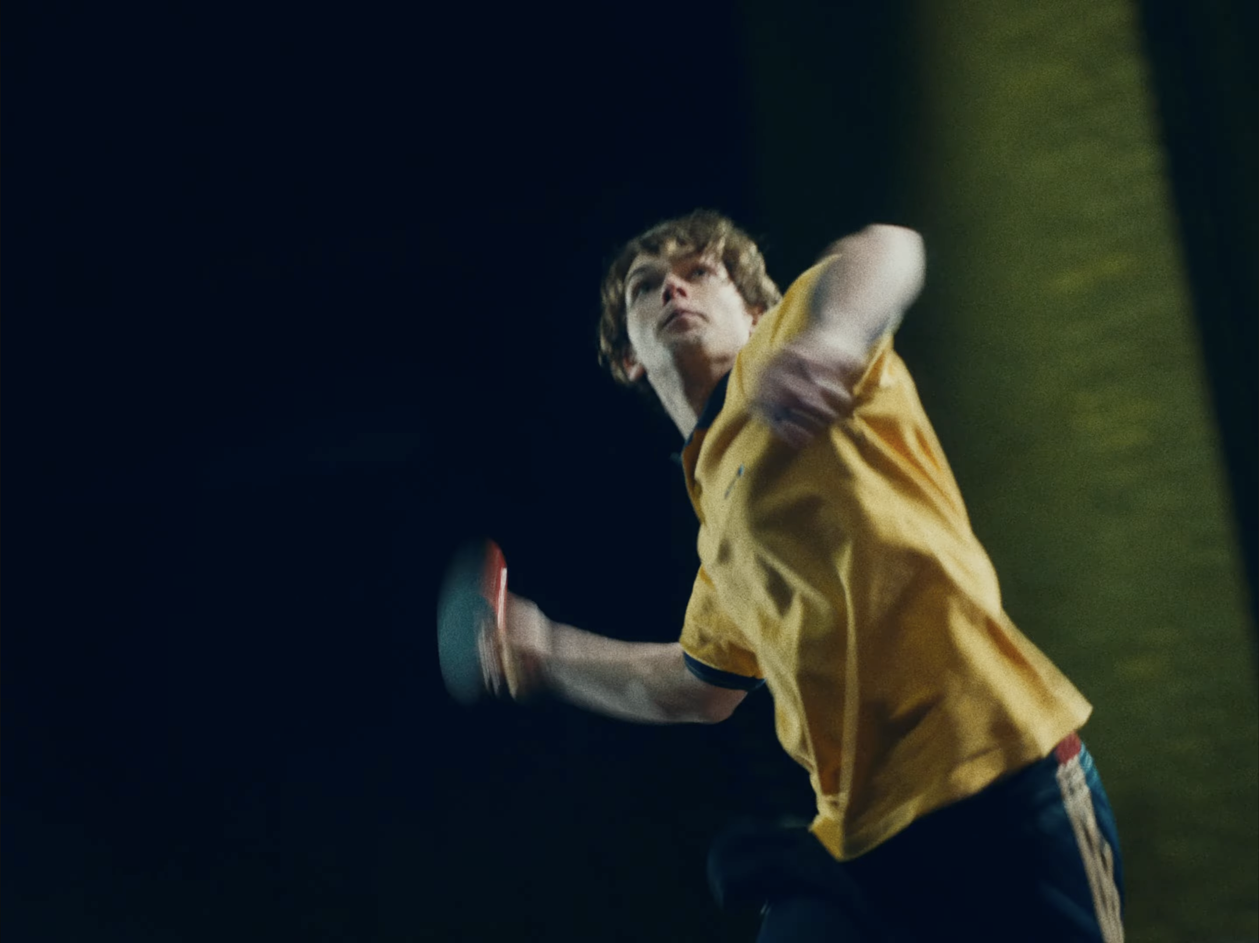 A young boy in a yellow jacket playing table tennis.