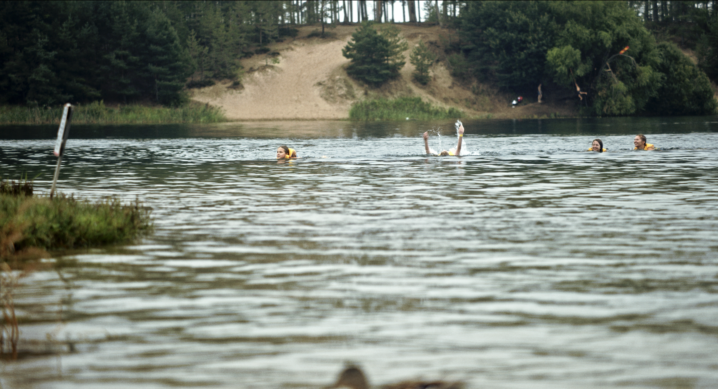 People swimming in a lake with a wooded hillside in the background
