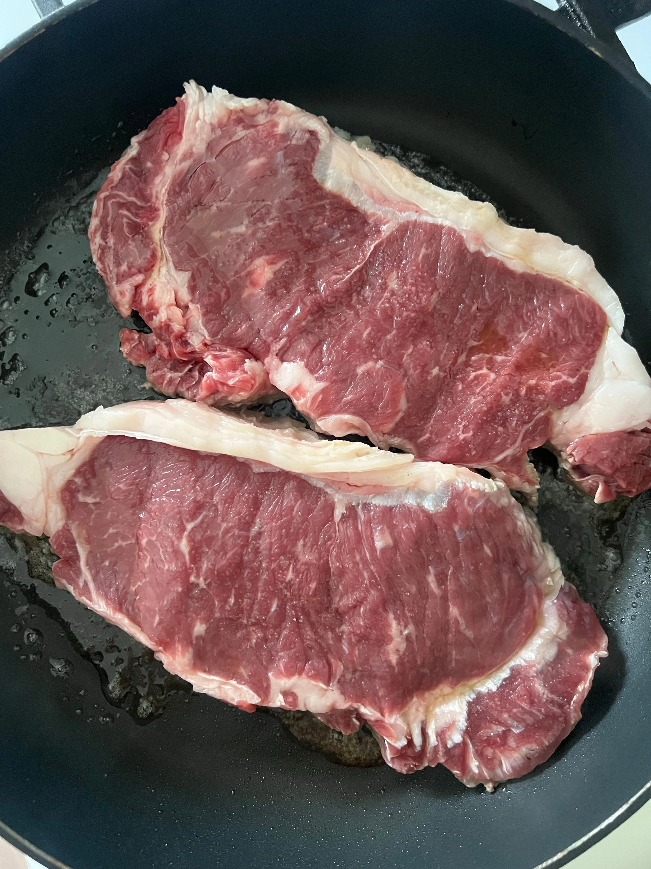 Two raw beef steaks in a black frying pan.