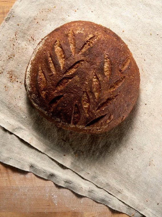 Round loaf of bread with decorative scoring on top, resting on parchment paper.