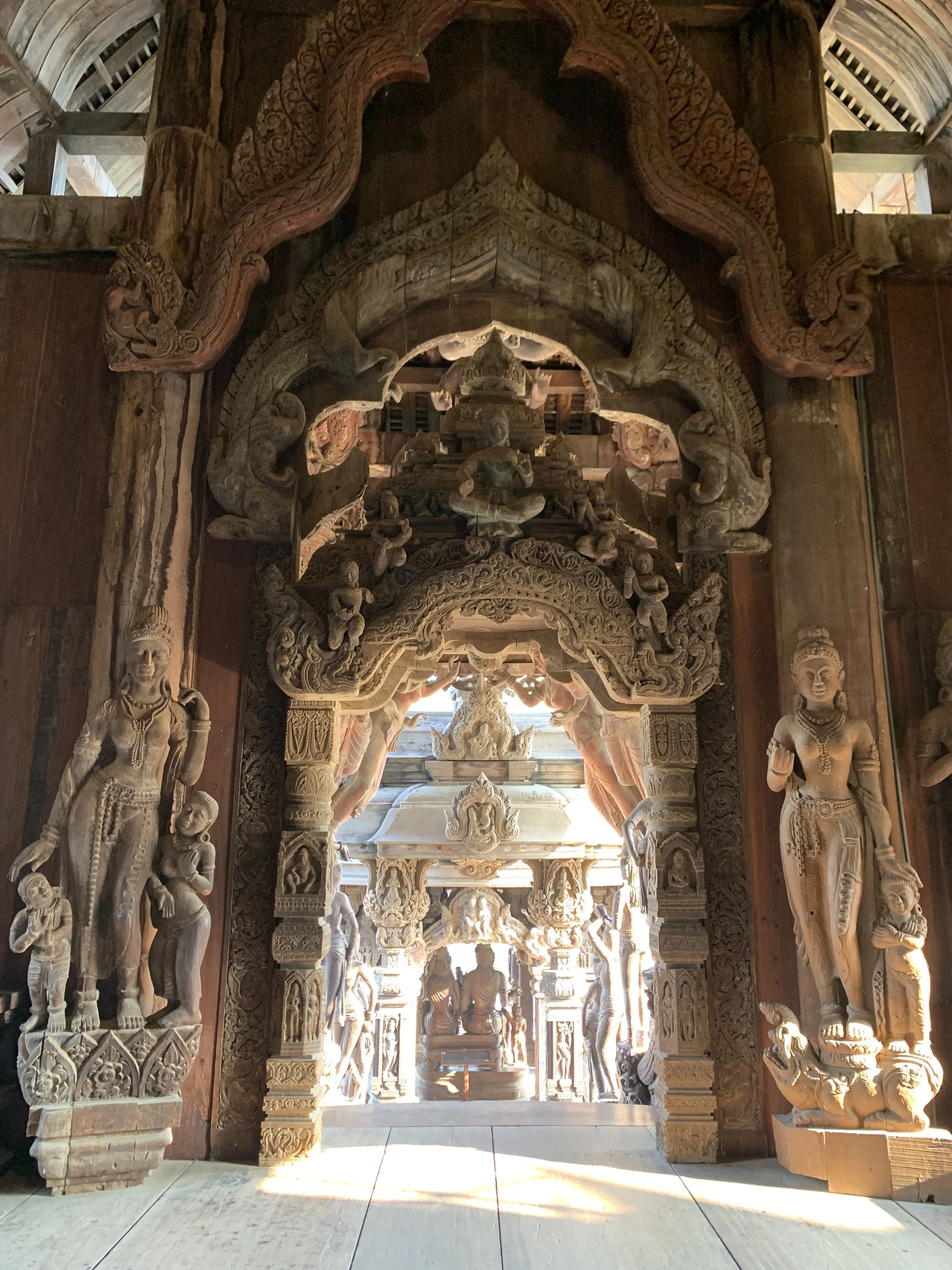 Portail en bois sculpté avec des figures mythologiques et des motifs détaillés, intérieur d'un temple ou d'une structure religieuse en bois sculpté.