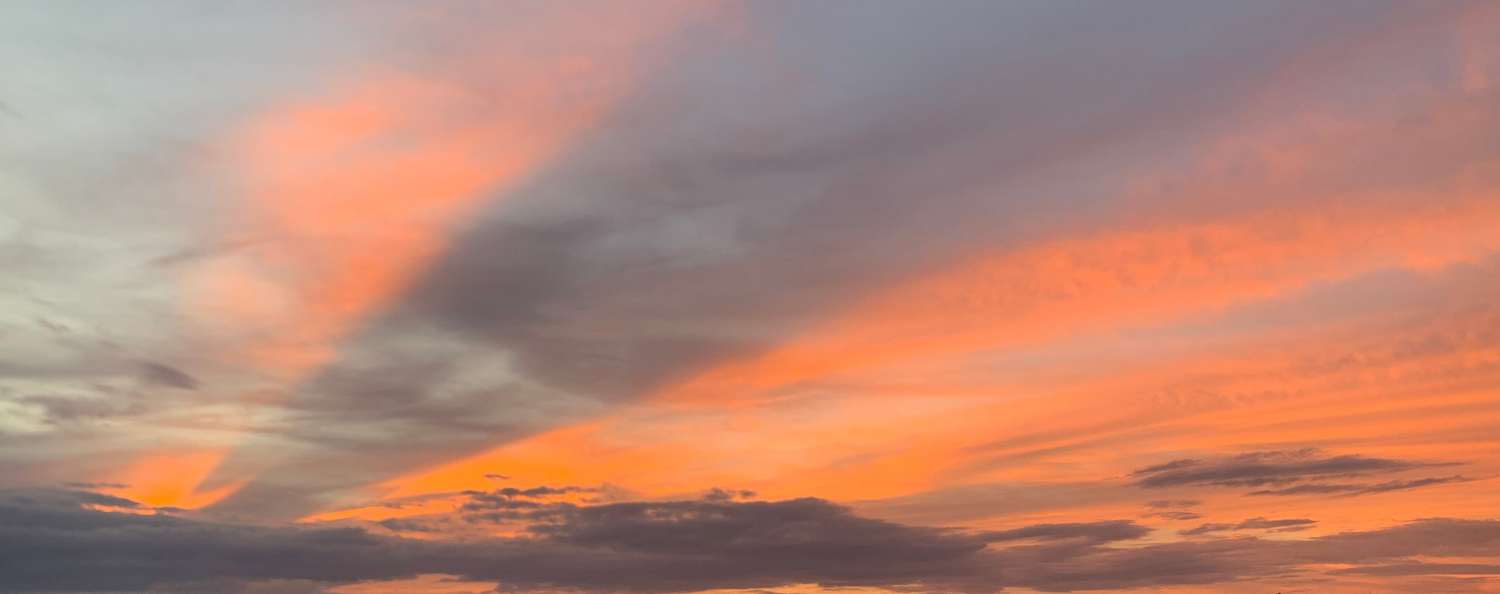Ciel de coucher de soleil avec des nuages roses, orangés et gris.