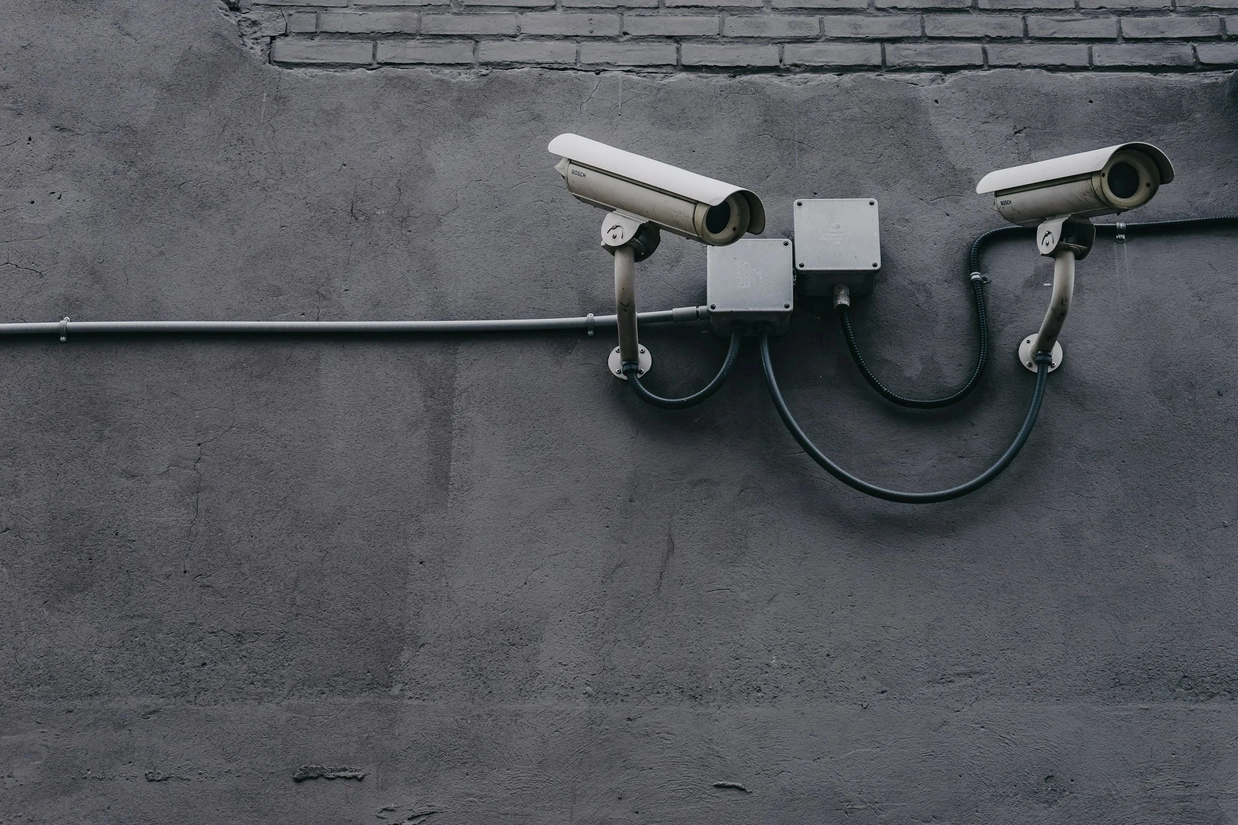 Two security cameras mounted on a gray concrete wall, with wires connected to a metal electrical box.