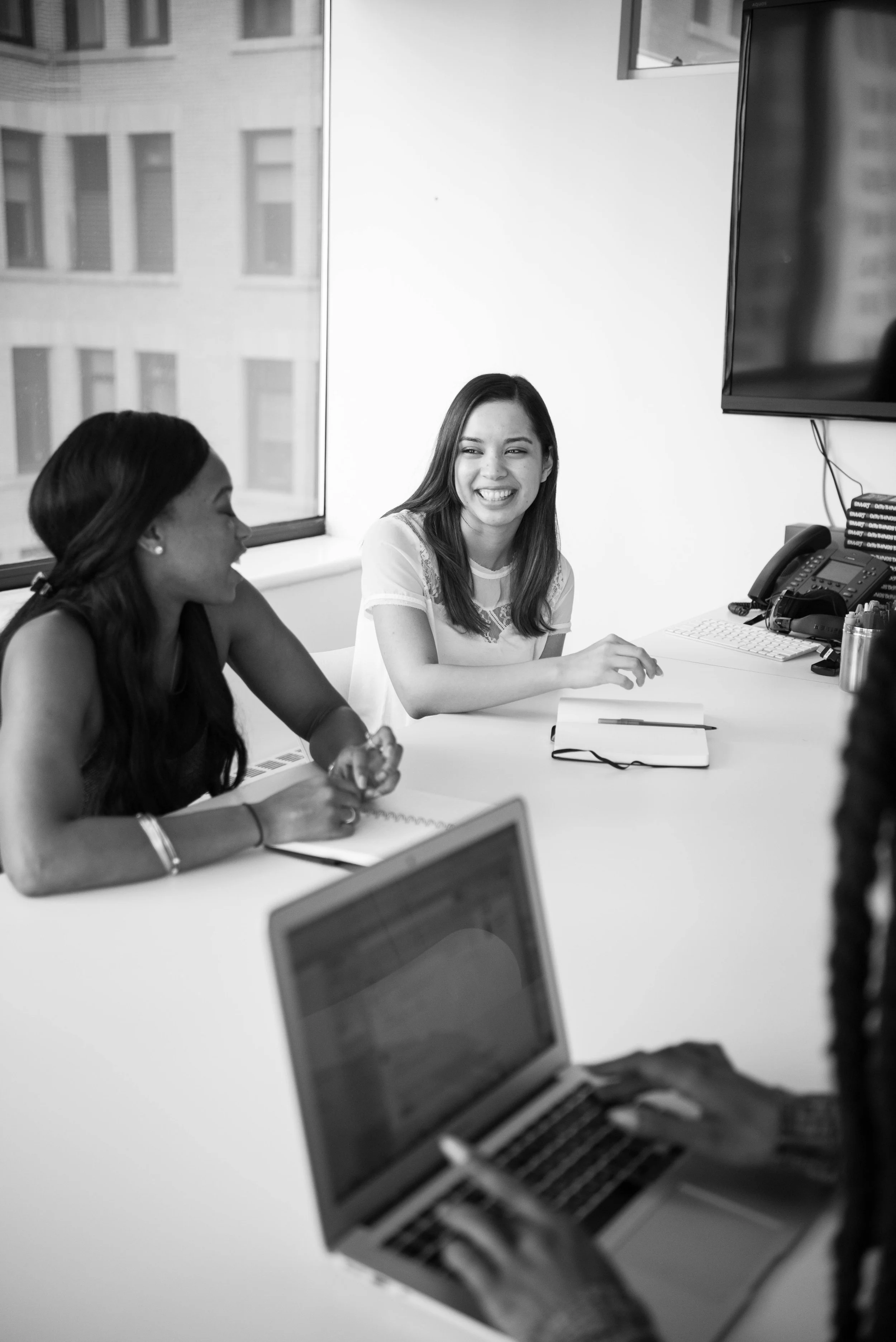 People in a meeting room discussing, with laptops and notebooks on the table.