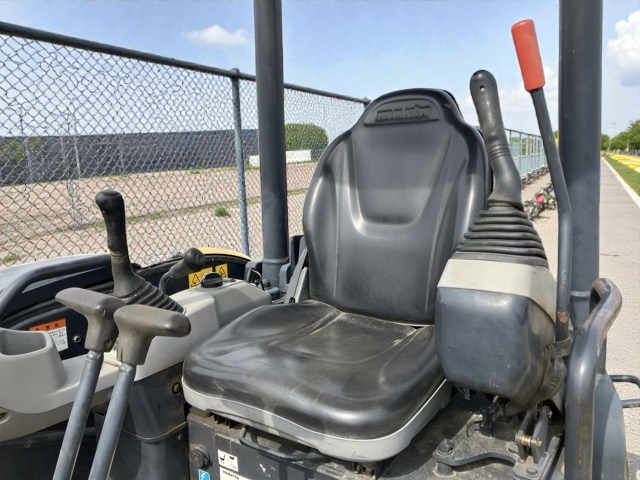 Front view of a construction vehicle's operator seat and controls, including steering levers and a large black seat, outdoors on a sunny day.