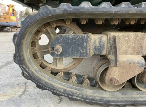 Close-up of a tracked excavator's rubber track and undercarriage, showing dirt and wear.