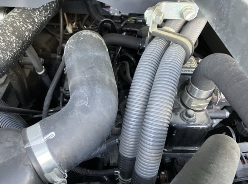 Close-up of an engine with large rubber hoses, metal clamps, and electrical wiring, part of vehicle's cooling and air intake system.