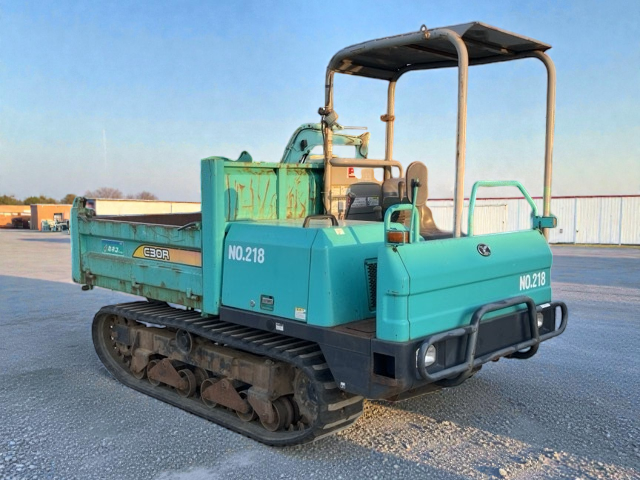 A small, turquoise construction or utility vehicle equipped with caterpillar tracks, a cargo area, safety rails, and an open canopy.