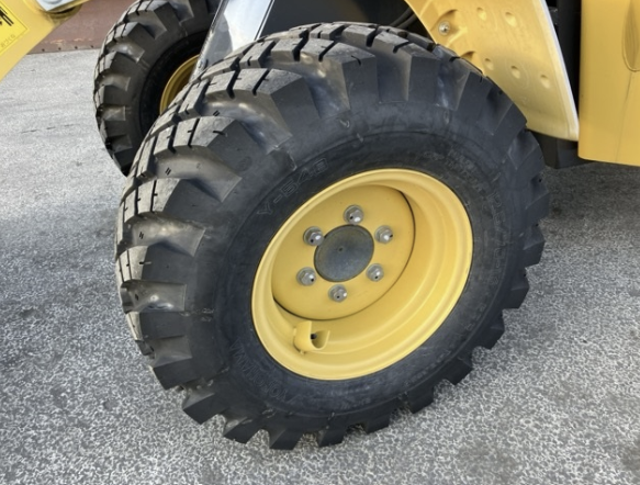 Close-up of a large black off-road tire mounted on a yellow vehicle, parked on asphalt.
