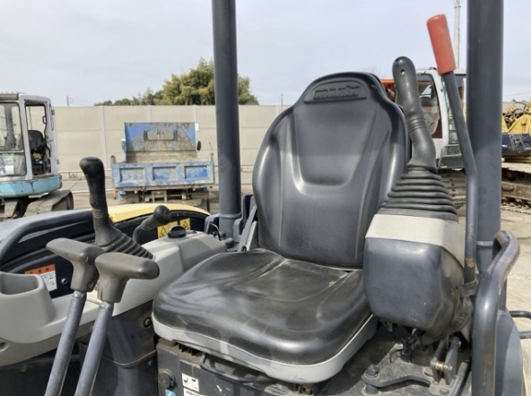 Construction vehicle seat with control levers and steering, outdoors in a yard.