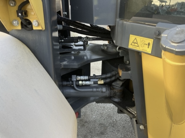 Close-up of construction equipment hydraulic system with hoses and warning label.