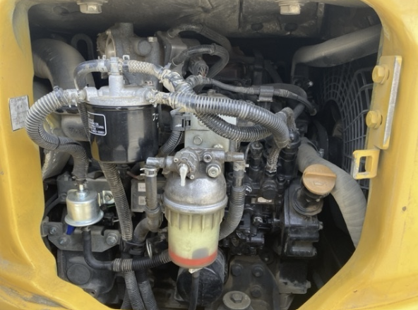 Close-up view of a yellow construction equipment engine with various hoses, filters, and components visible.