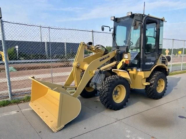Yellow Komatsu front loader parked on sidewalk, fenced area in background