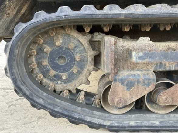 Close-up of a dirty rubber track on a small excavator or bulldozer, showing the metal rollers and undercarriage components.
