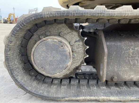 Close-up of a tracked construction vehicle's track and sprocket wheel, with dirt and dust on the metal parts.
