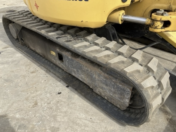 Close-up of a yellow construction vehicle's rubber track, showing wear and dirt on the track and metal undercarriage.