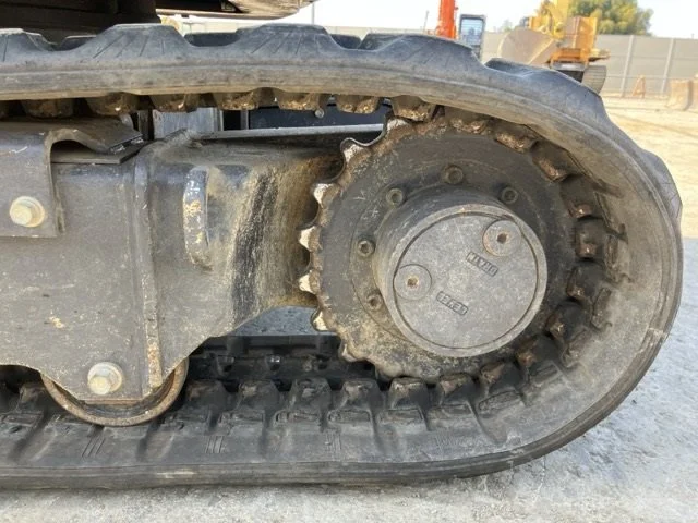 A Komatsu mini excavator parked on a paved surface near a chain-link fence with a body of water and green landscape in the background.