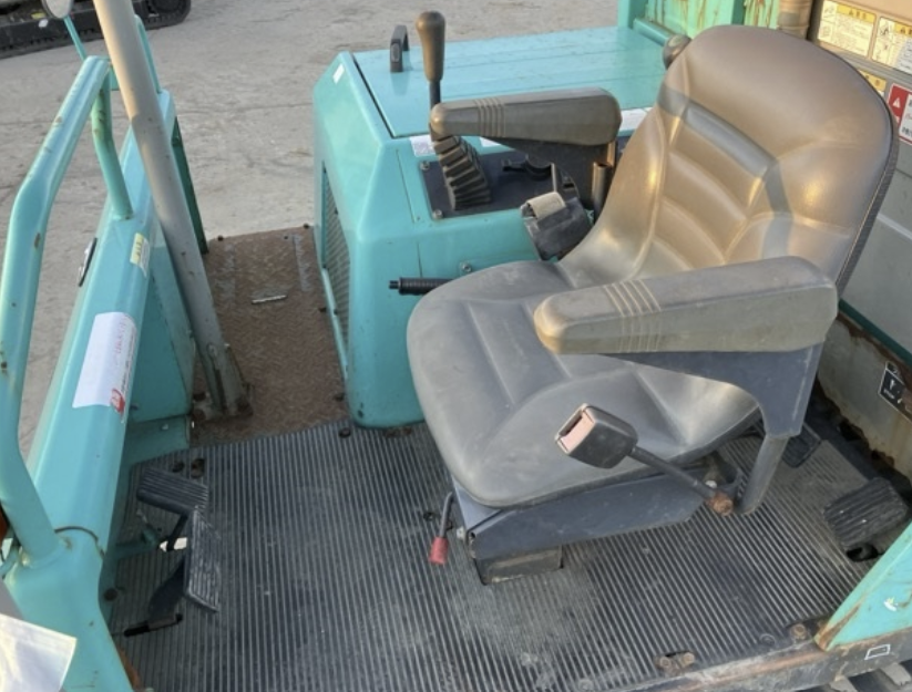Interior of a teal-colored industrial or construction vehicle with a gray cushioned seat, steering wheel, and various control levers.
