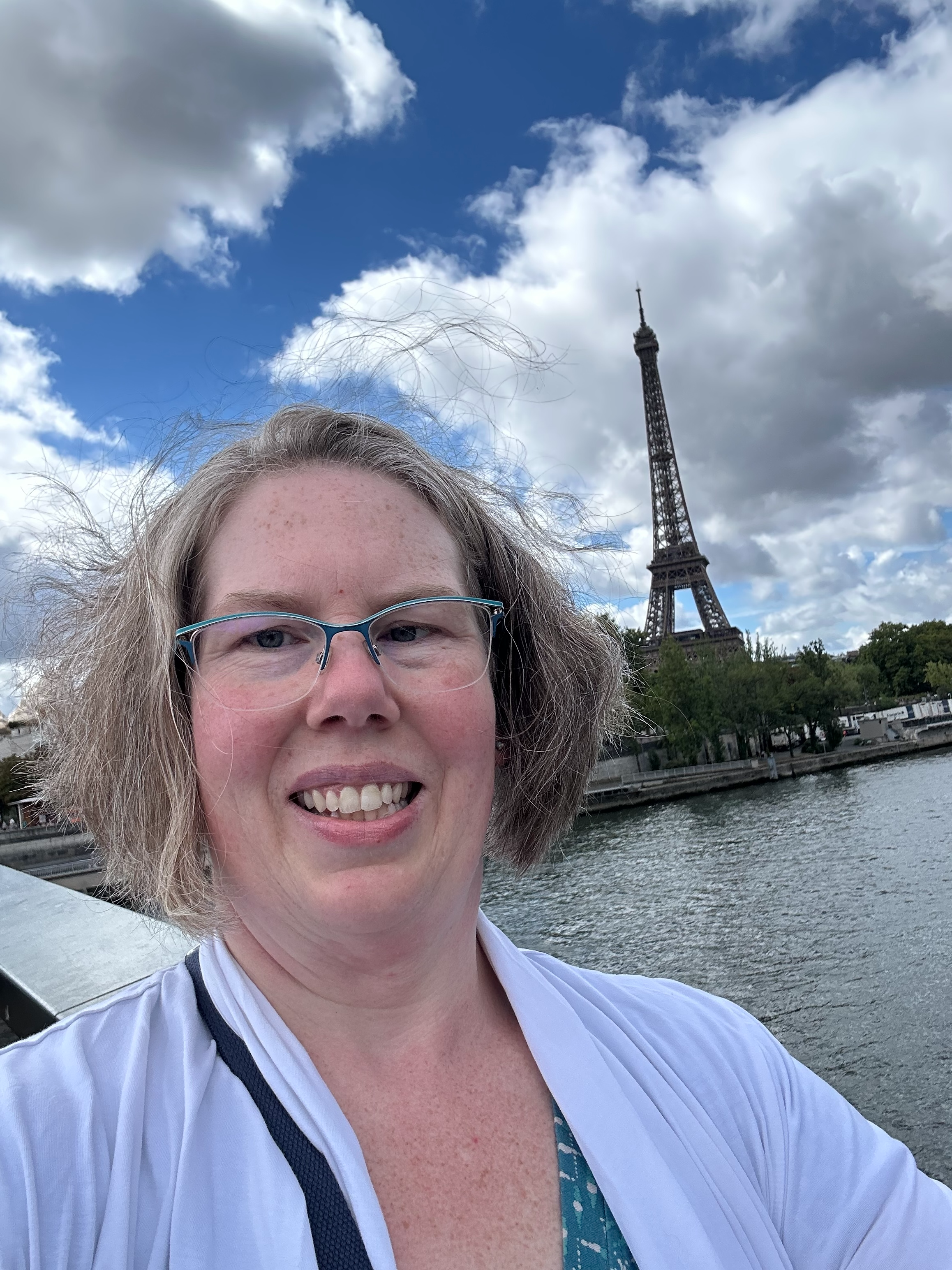 Tara Sedov smiling in a windswept selfie along the Seine, with the Eiffel Tower in the background