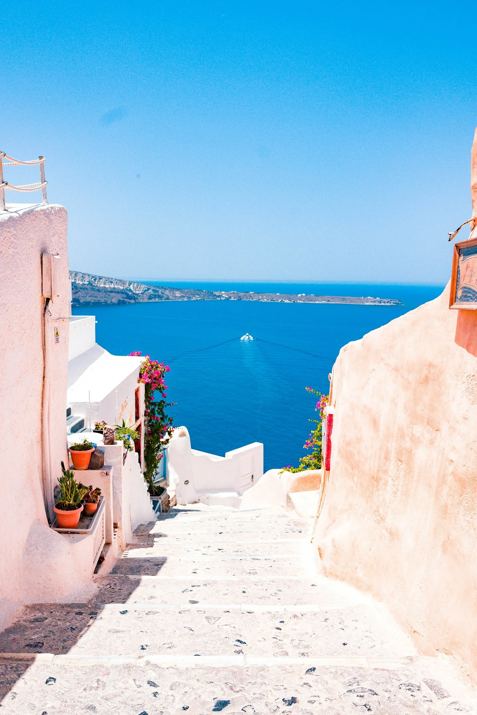A scenic view of a Greek island with whitewashed buildings along a narrow stairway, overlooking the blue sea and sky.