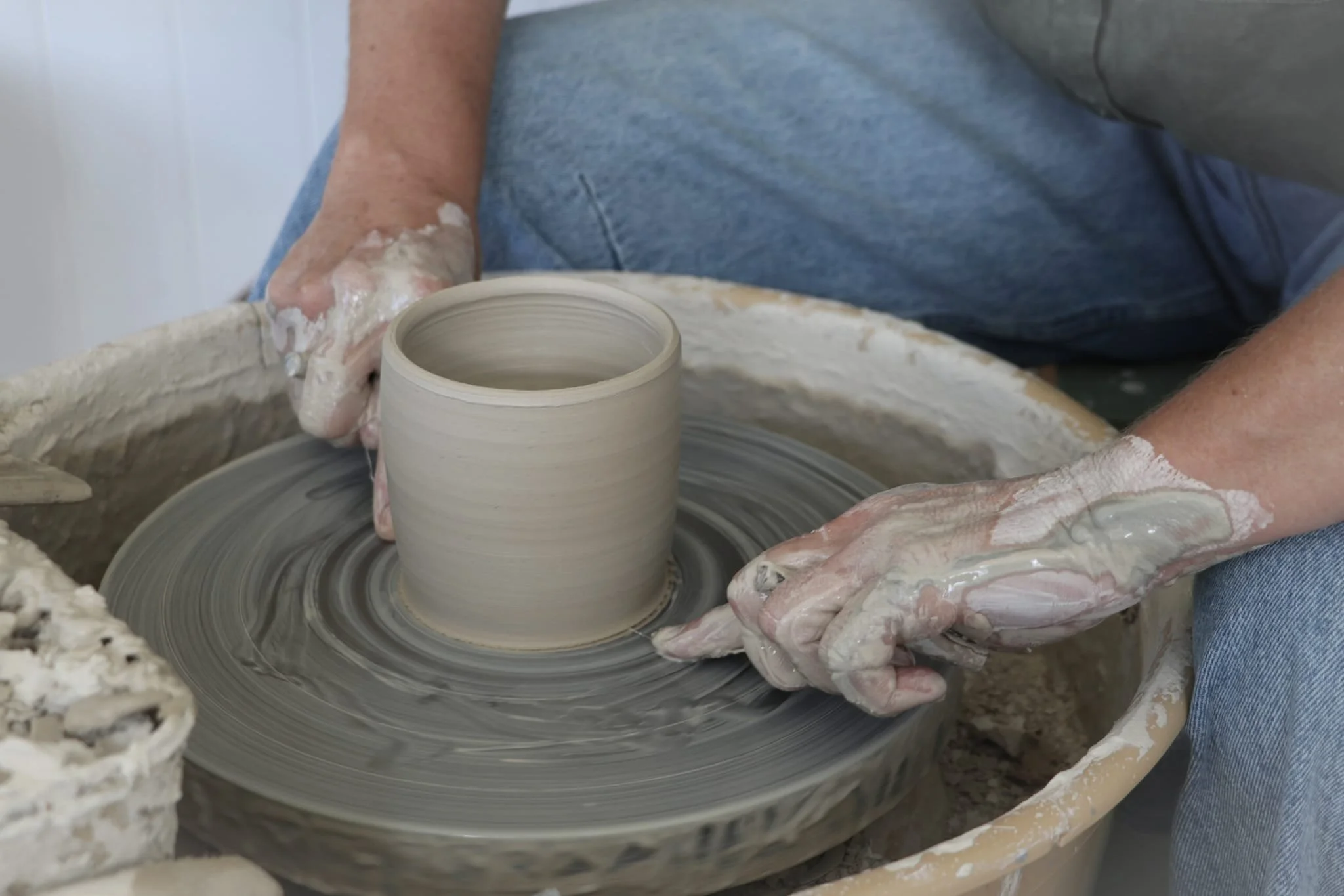 A person shaping a clay pot on a pottery wheel, mindfulness, sensory and grounding pottery techniques.