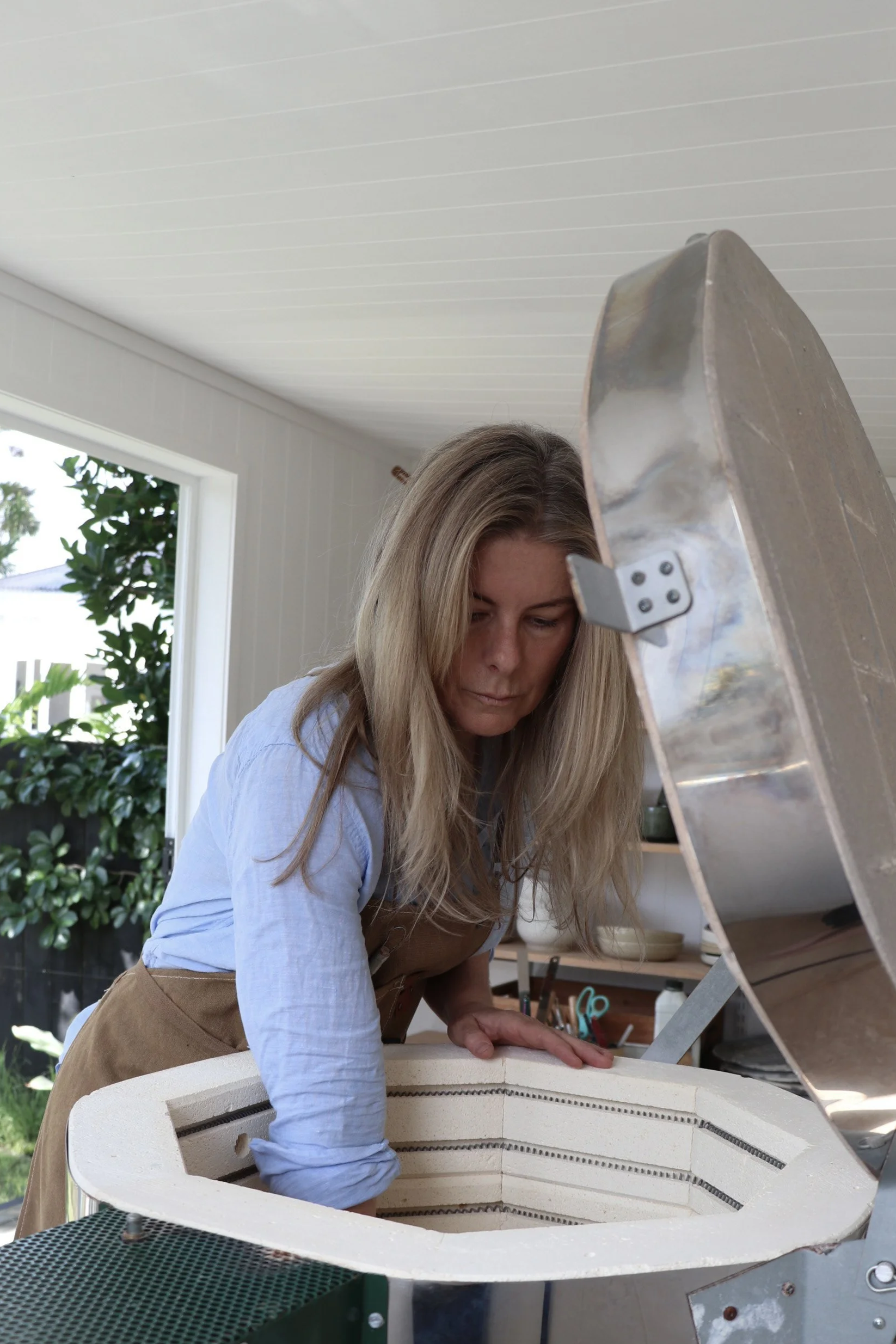 New Zealand ceramic artist emptying the kiln in a modern, design-led studio with a lush garden outside.