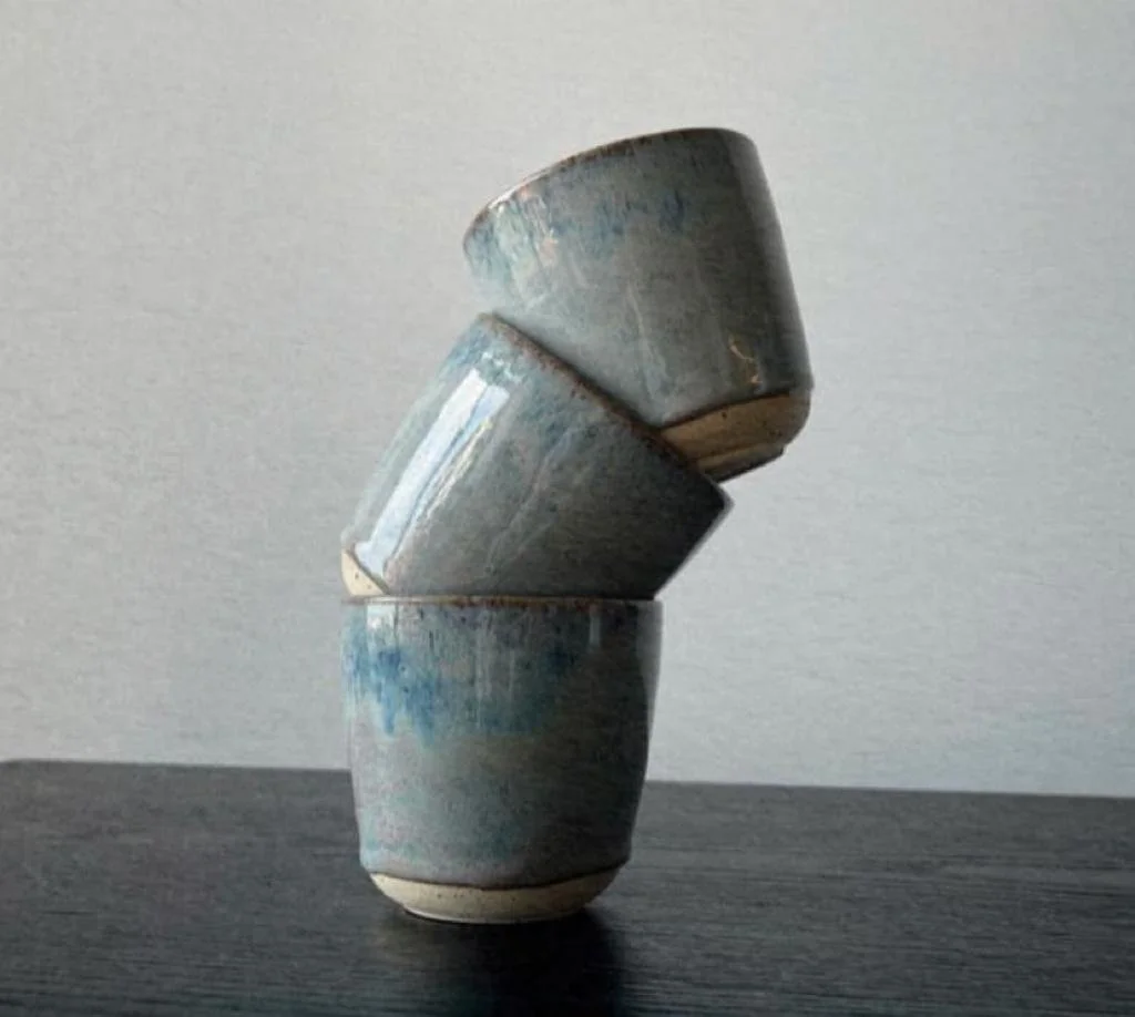 Three ceramic cups stacked in a balancing formation on a dark surface with a plain light-colored background.