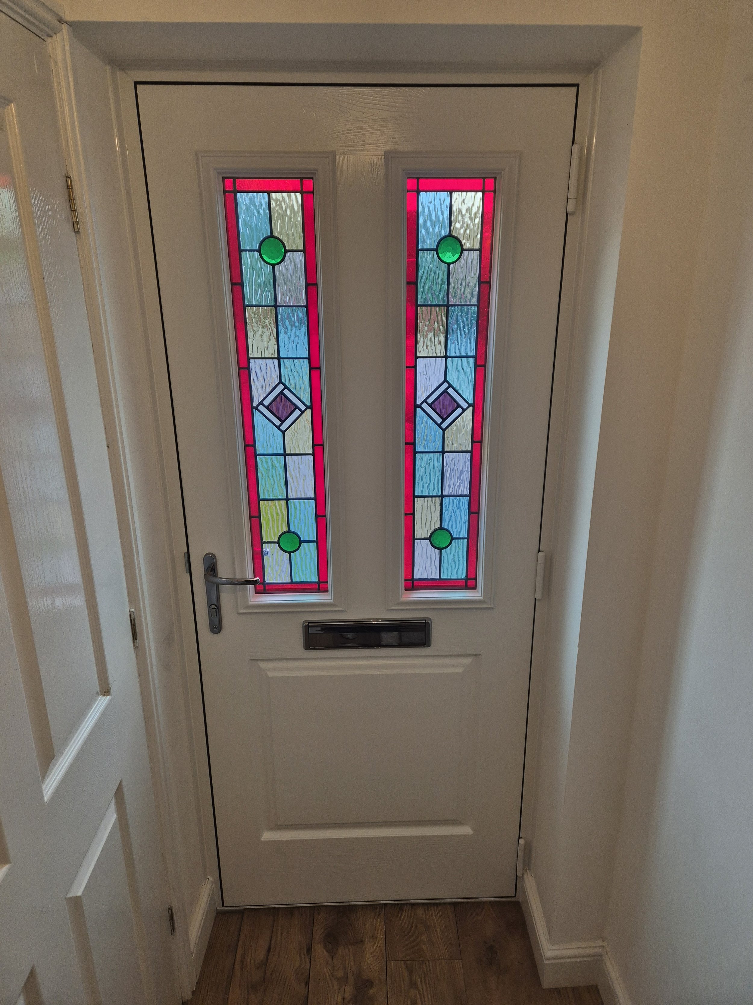 Internal hallway view of timeless composite front door featuring colourful stained glass panels that flood the space with light.