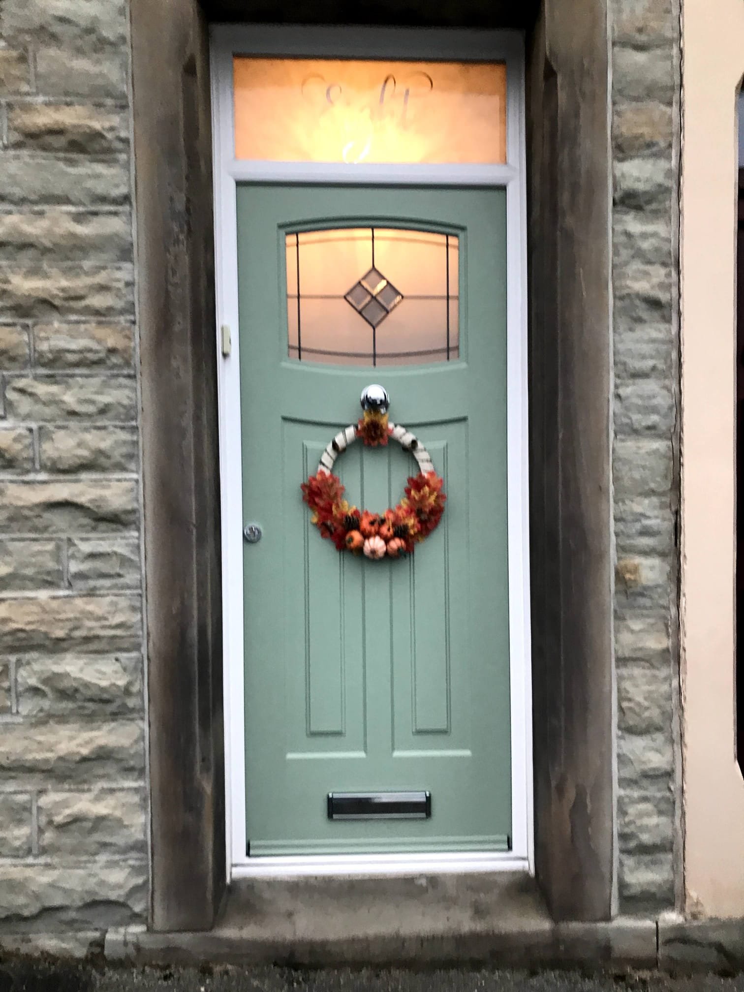 Chartwell Green Rockdoor featuring an elegant decorative glass panel, a crisp white outer frame, and a bespoke overhead fanlight. The custom fanlight has the house number precision-etched into premium satin glass.