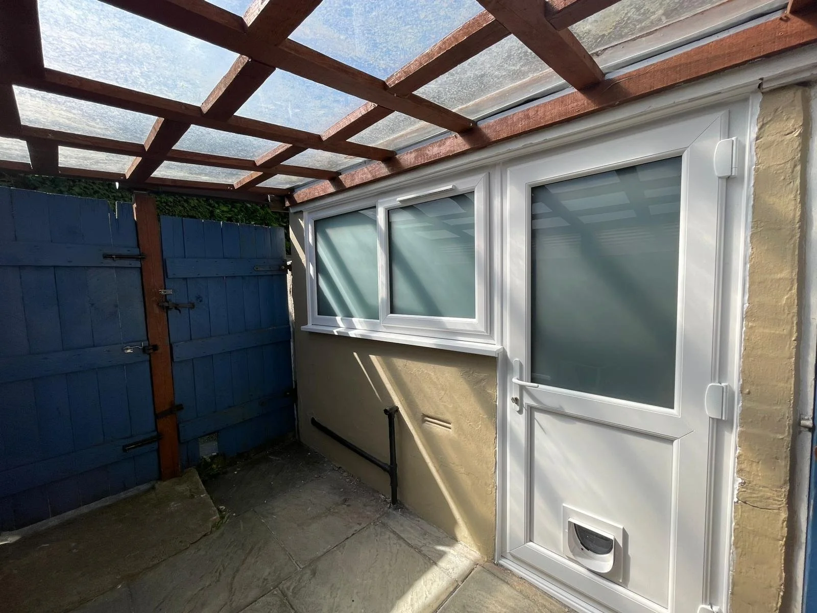 White PVC back door featuring an integrated cat flap, installed alongside matching PVC windows for an outbuilding. Satin glass panels in the door and windows ensures complete privacy.