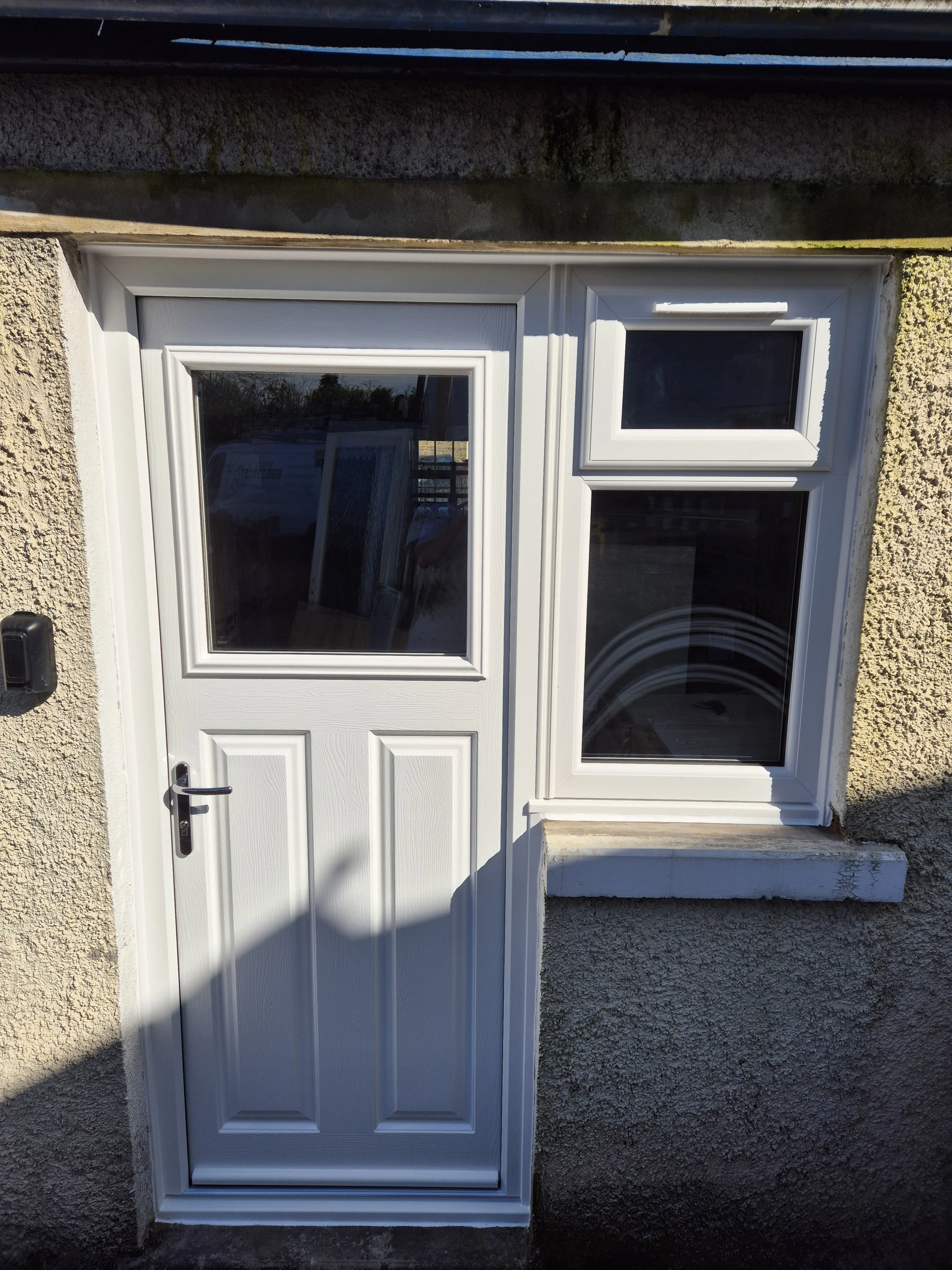 White composite back door featuring a realistic wood-grain effect and an integrated matching side window. The large clear glass panel floods the rear entrance with natural light while providing exceptional thermal efficiency.