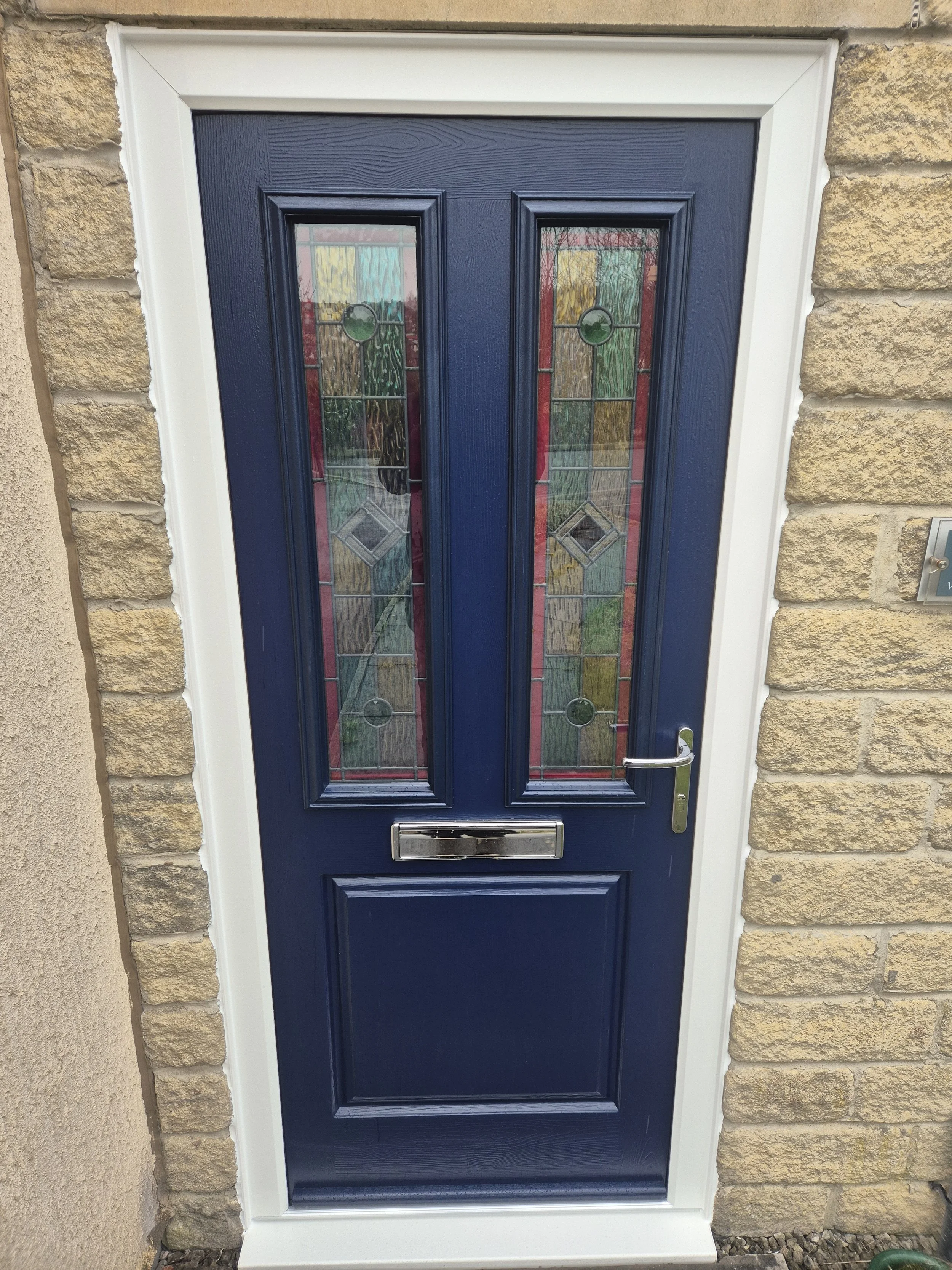 A timeless Royal blue composite front door featuring decorative stained glass panels. Finished with a crisp white frame and silver hardware, it creates a beautiful, characterful contrast against the beige brick exterior.