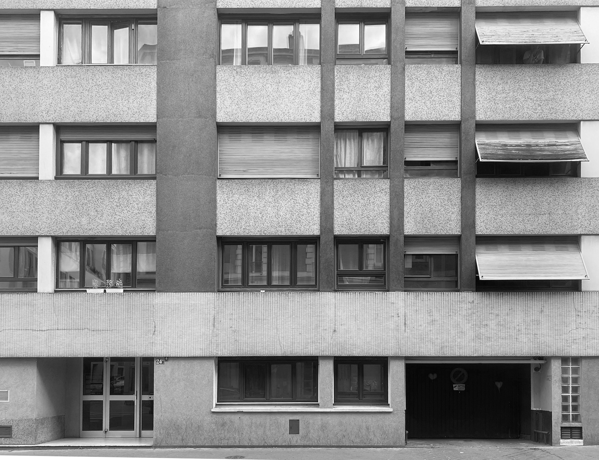 Façade d'un immeuble résidentiel avec plusieurs fenêtres et volets, en noir et blanc.