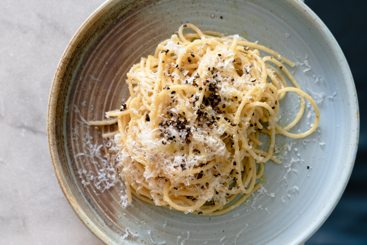 A bowl of cooked spaghetti topped with shredded cheese and black pepper.