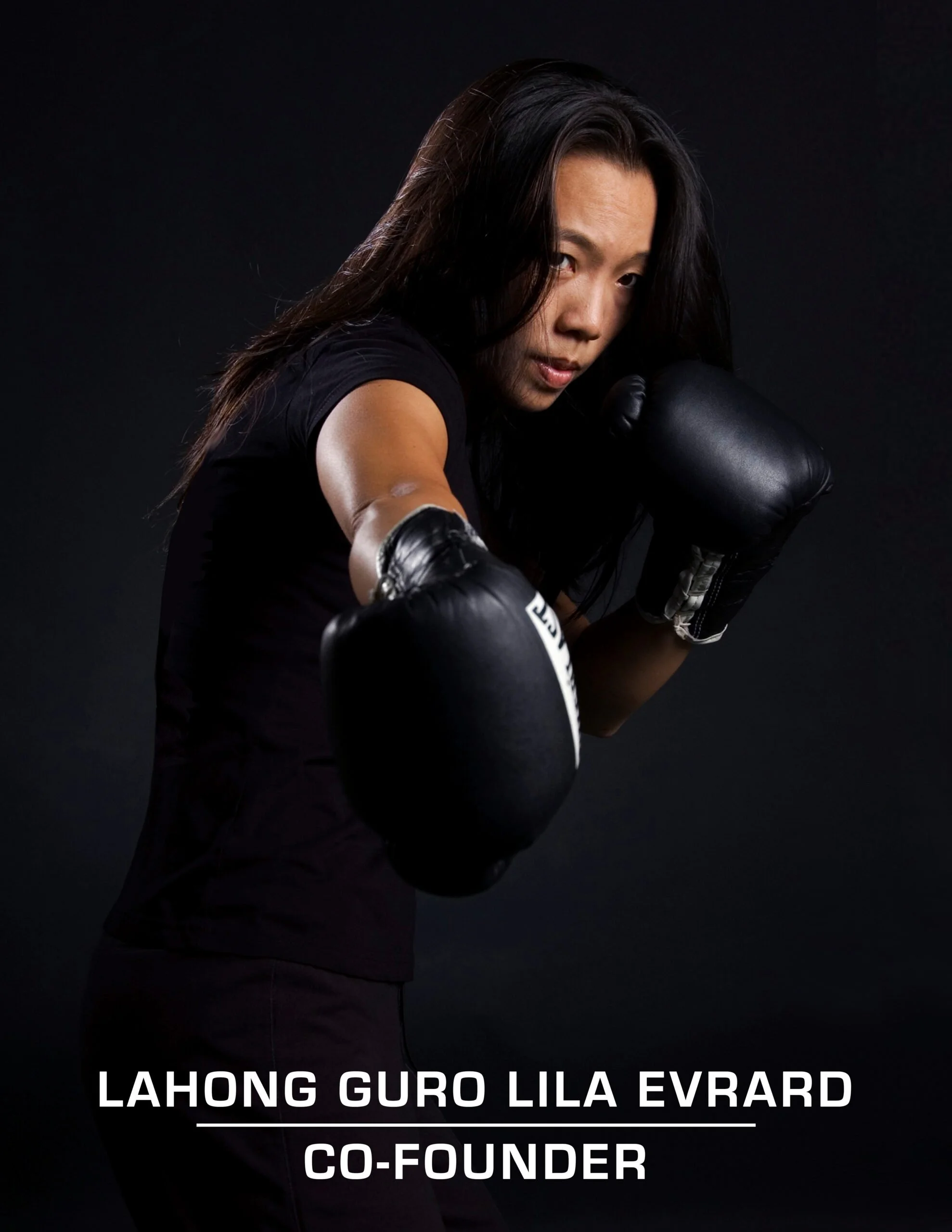 Professional woman boxer in black gloves and sportswear, posing with her fists up in a dark studio. Text overlay reads: 'Lahong Guro Lila Evrard, Co-Founder'.