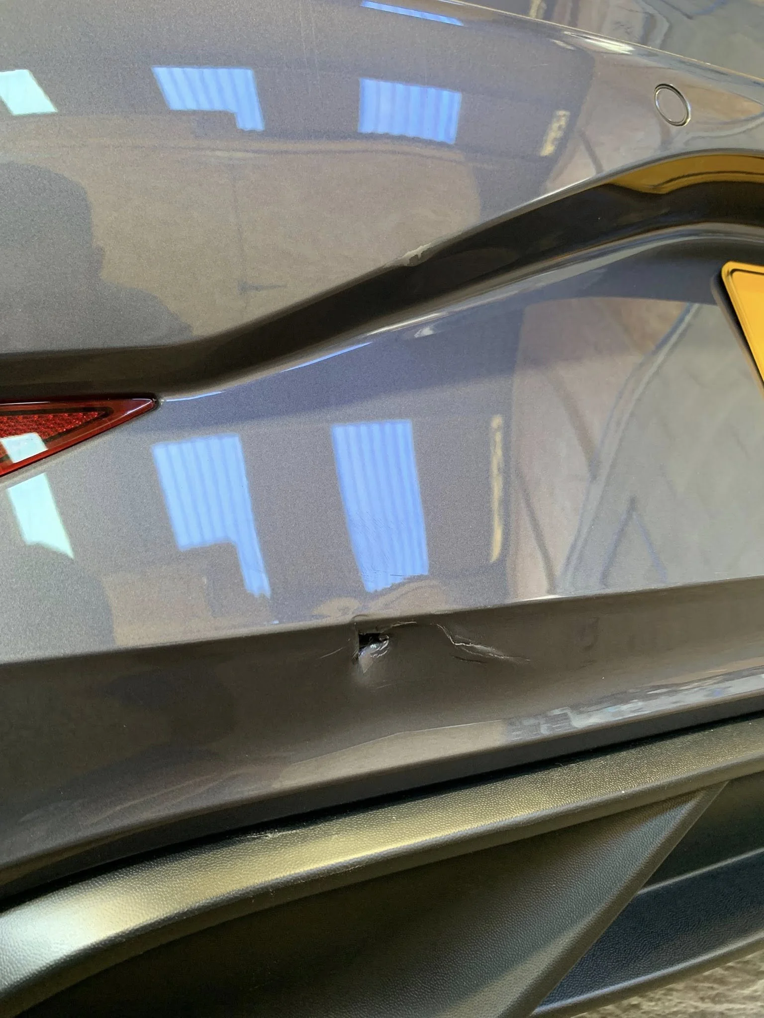 Close-up of a gray car with a dent and scratch on the rear bumper.